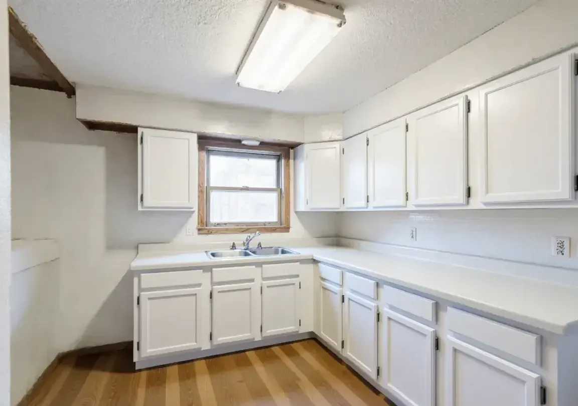 the same kitchen with white cabinets, new counters and a wood-look floor
